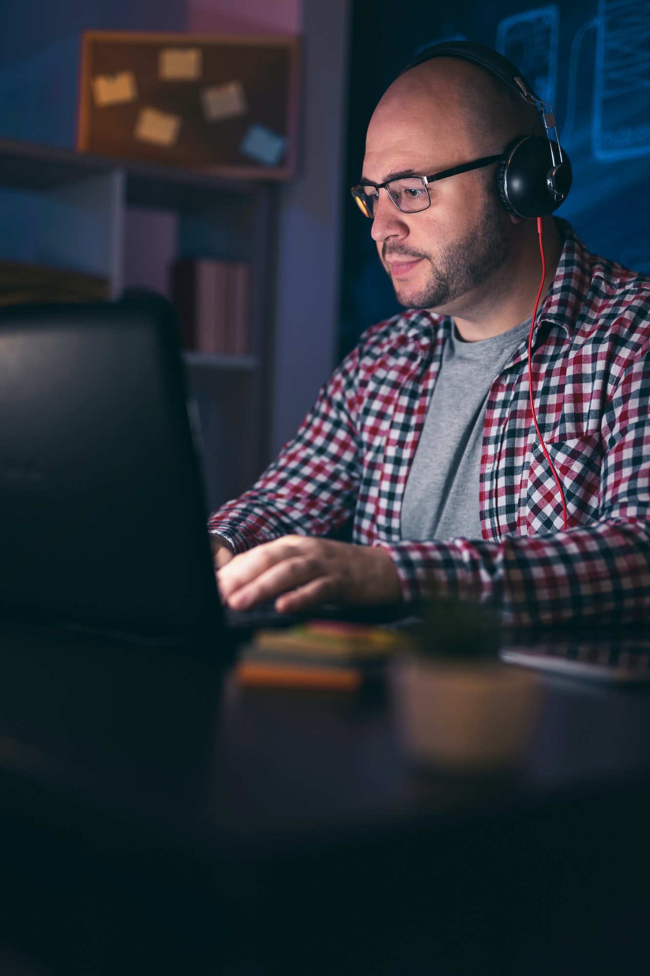 Man wearing headset using laptop computer while working overtime
